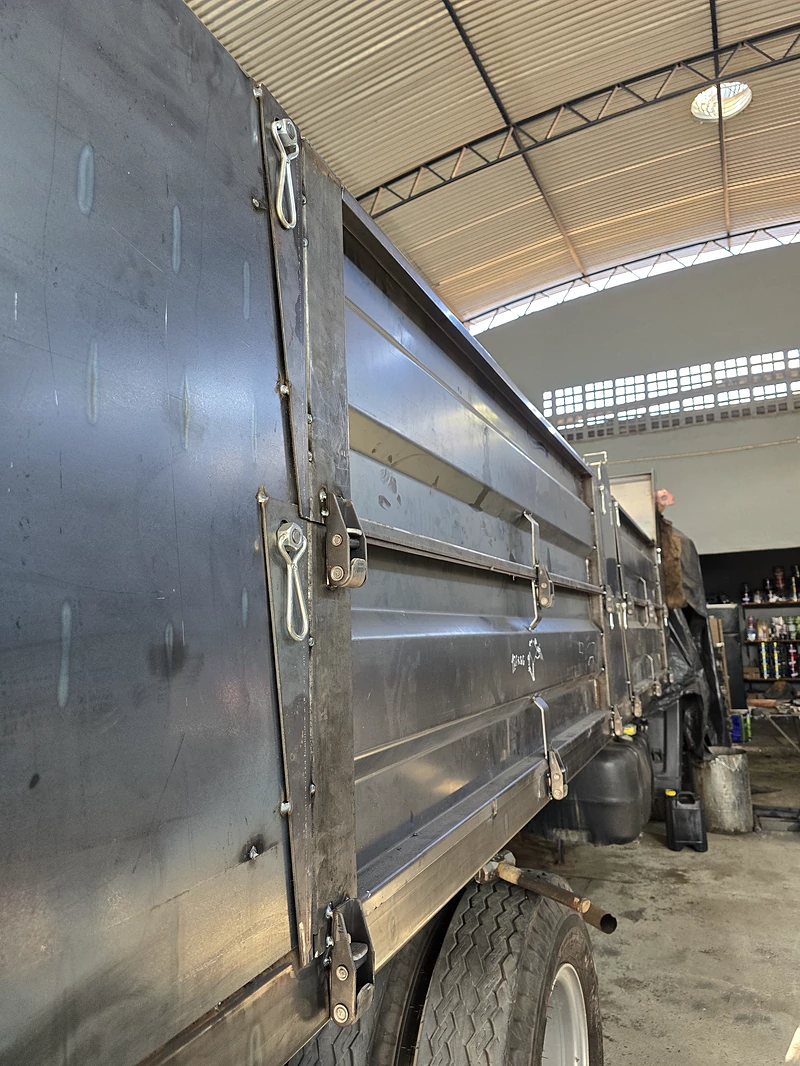 Lateral de caçamba em aço sem pintura, com os vincos da dobra, o fecho de alavanca e o olhal de amarração