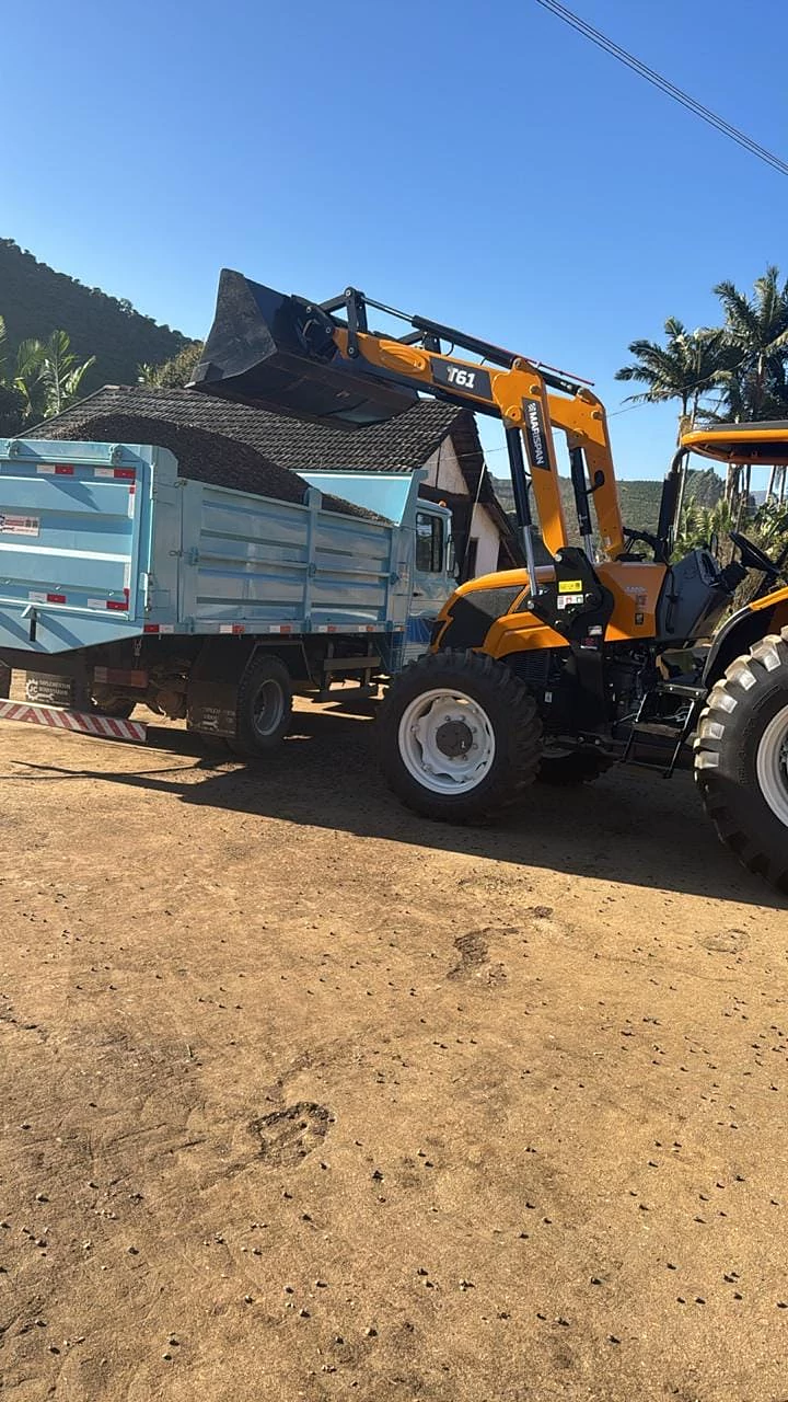 Caçamba sendo carregada por uma máquina no campo