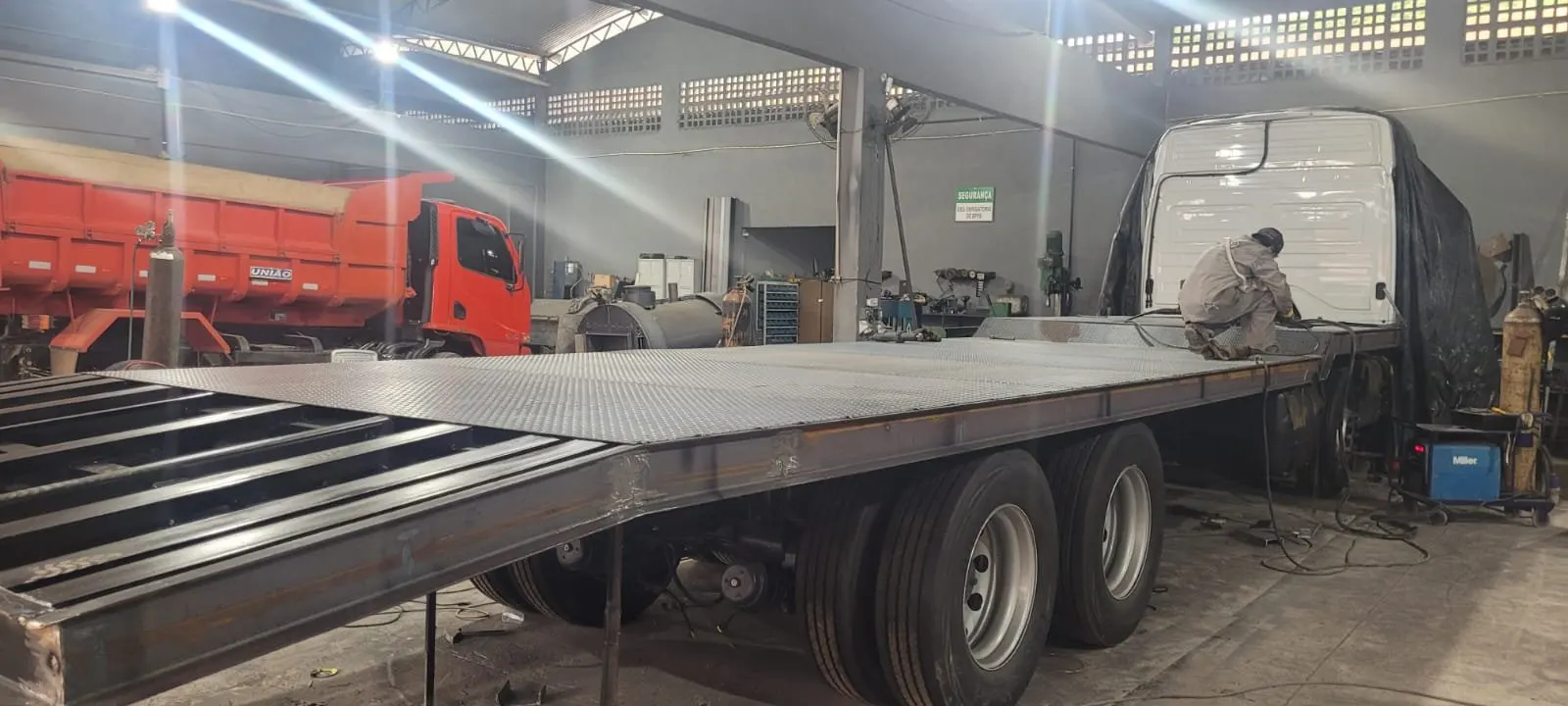 Caminhão em fabricação na oficina da JC, com trabalhador soldando a estrutura